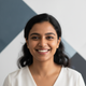 Portrait of a smiling South Asian woman, exuding confidence and contentment against a clean, minimalist backdrop.